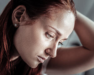 A red-headed woman looking sad looking off to the right side. Her head is leaning on her hand.